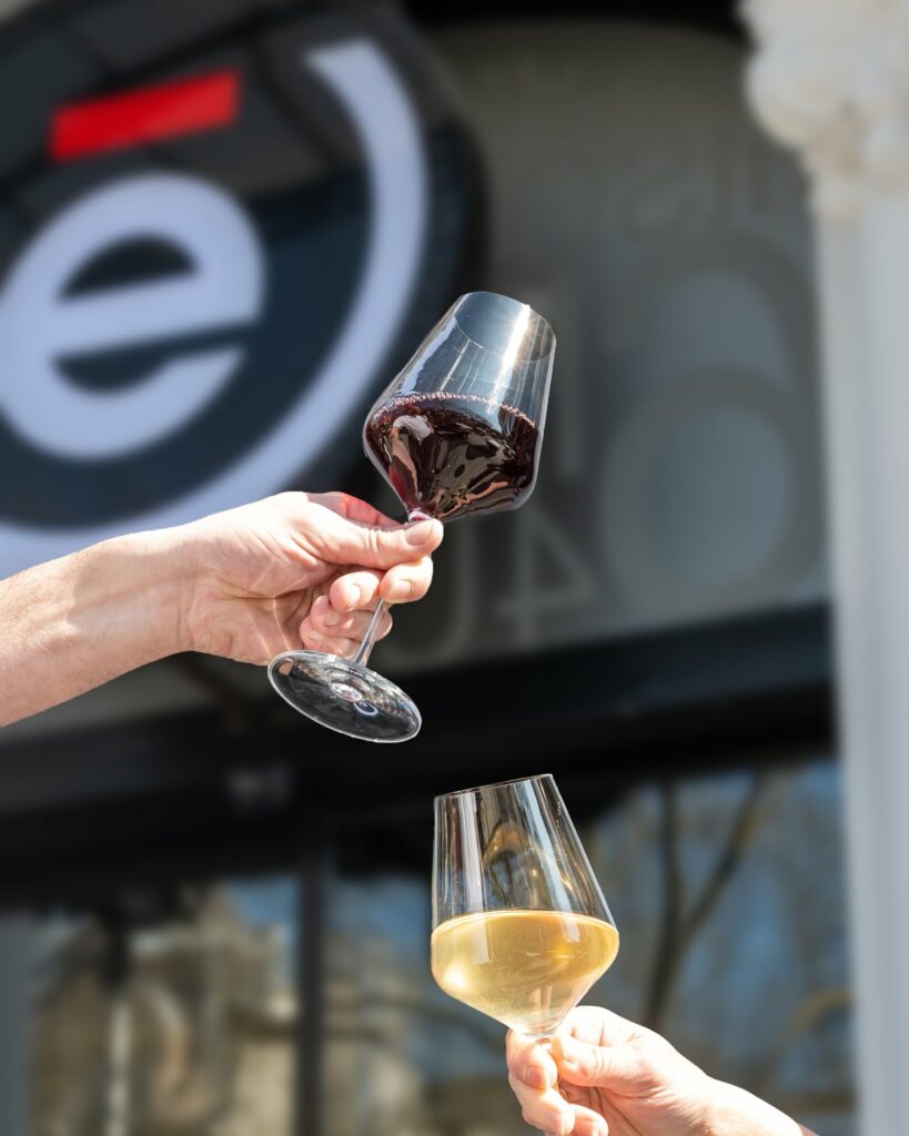 Deux verres de vin, un rouge et un blanc, trinqués en terrasse devant l’enseigne de L’Édito.